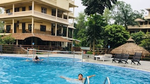 Piscina com espreguiçadeiras e um edifício ao fundo.