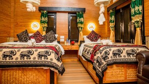 Quarto com duas camas, cada uma com roupa de cama estampada com elefantes, paredes de madeira e um candeeiro central.
