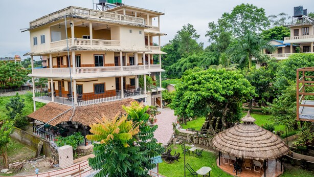 Um edifício de vários andares com varandas e um jardim com uma construção de telhado de palha.