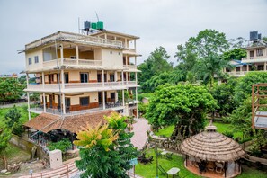 Un edifici de diverses plantes amb balcons i una zona de jardí amb una construcció de teulada de palla.