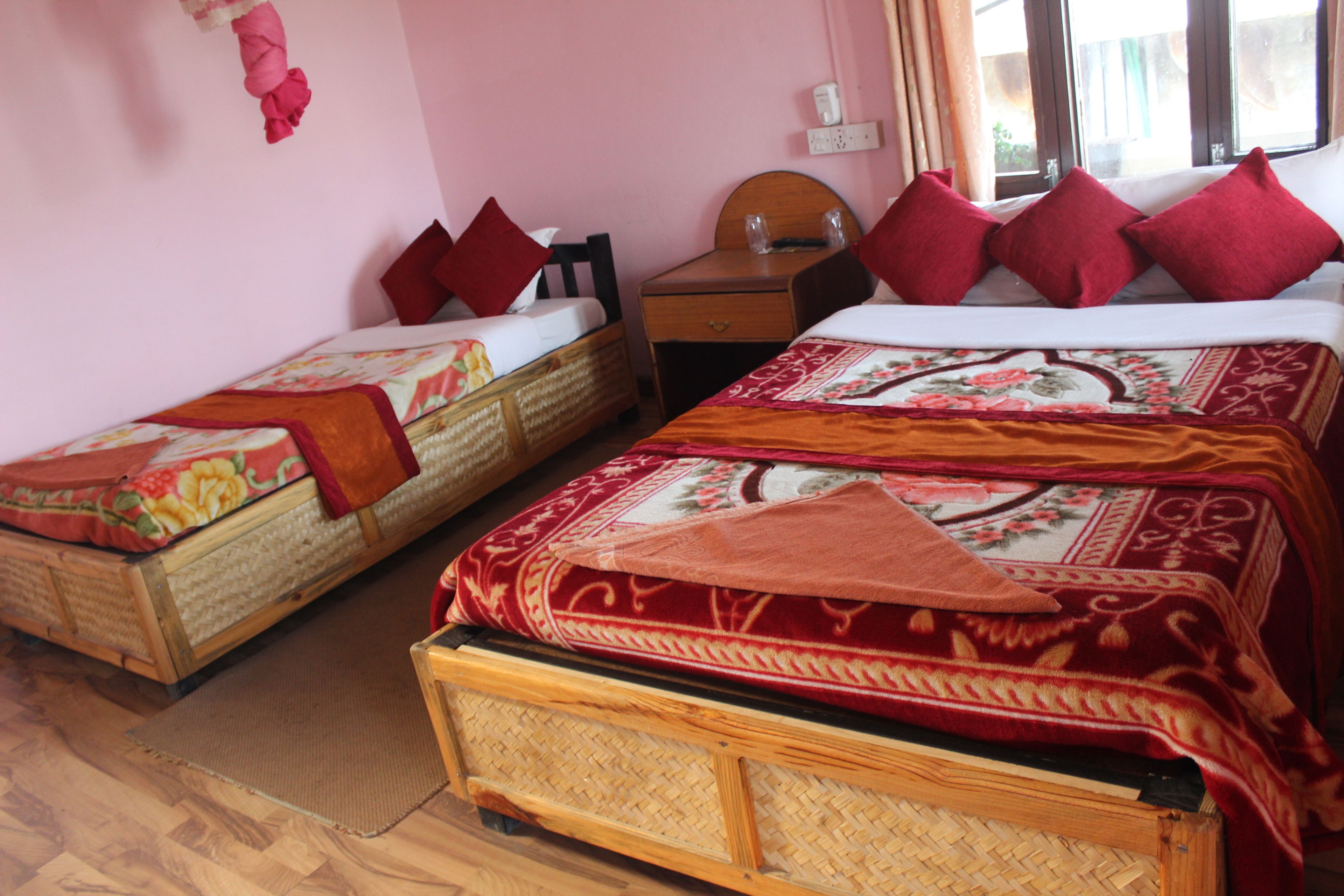 Una habitación con dos camas individuales, una mesita de noche de madera, una pequeña mesa y una ventana con cortinas.