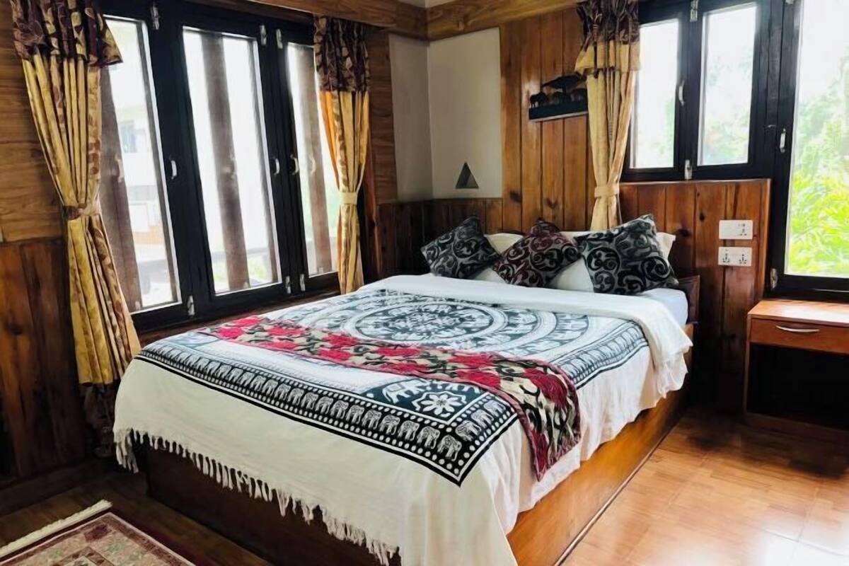 A wooden-paneled room with a bed, curtains, a bedside table, and a window.