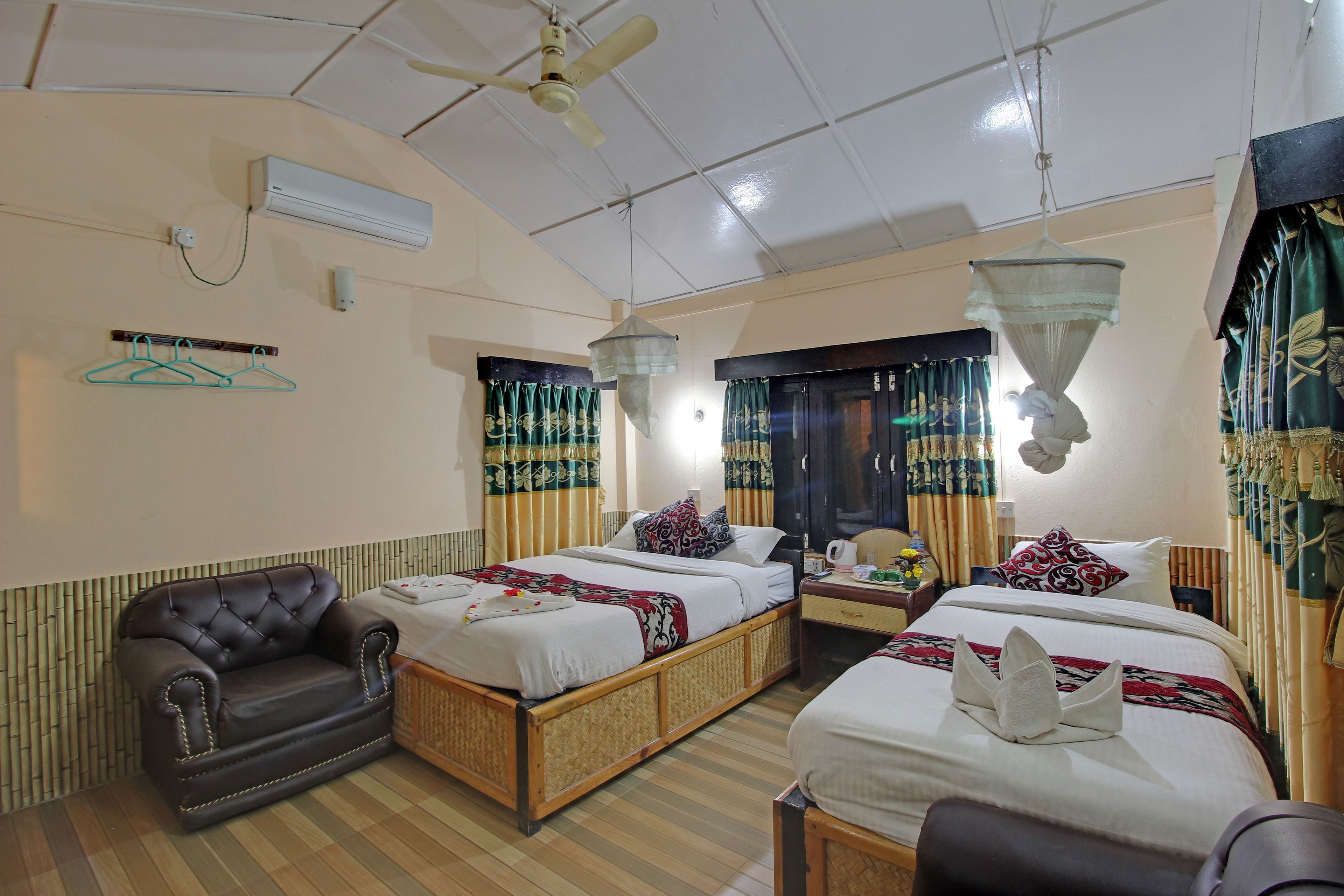 A hotel room with two beds, a sofa, a ceiling fan, an air conditioner, and a hanging light fixture.