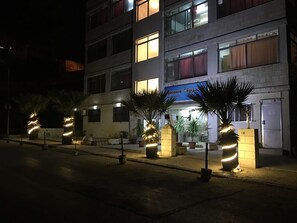 A hotel with multiple floors, illuminated windows, and potted plants in the entrance area. - Aljazeera Hotel Apartments (Amman)