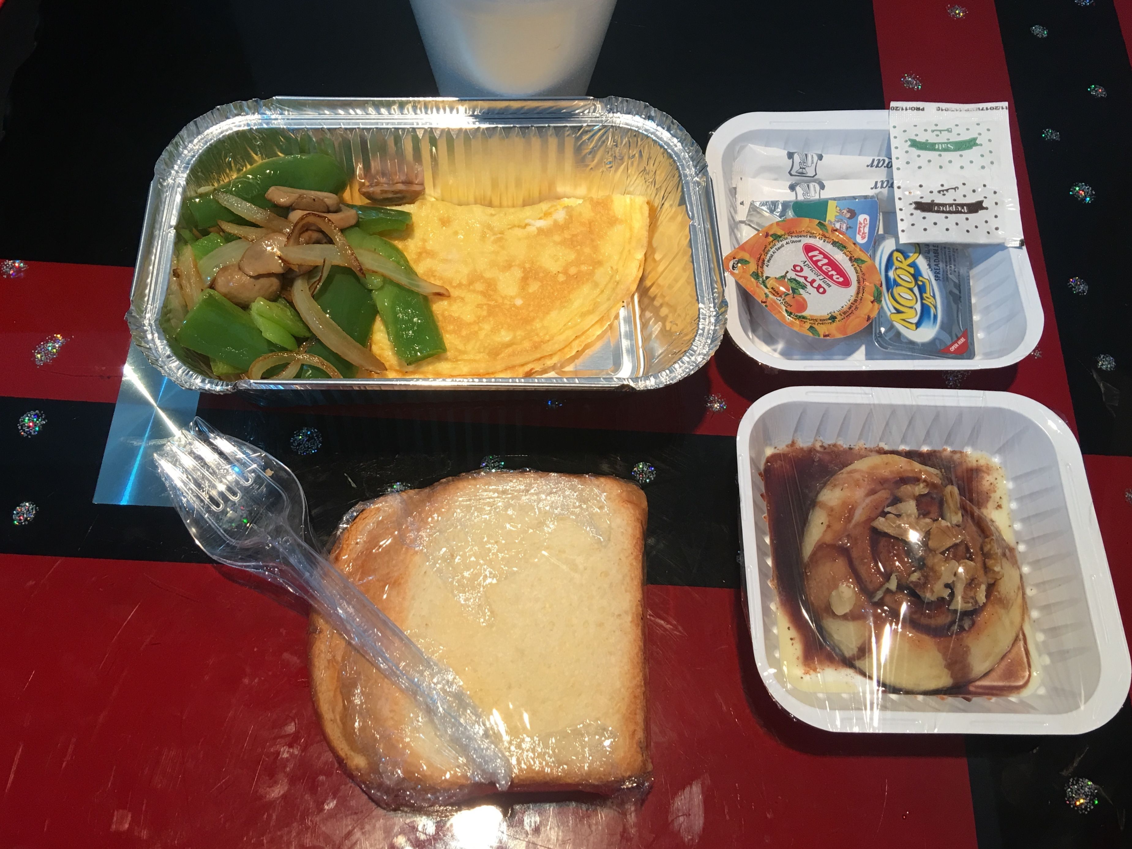 A meal with a foil container, a plastic fork, a slice of bread, and a plastic container with a dessert.