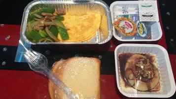A meal with a foil container, a plastic fork, a slice of bread, and a plastic container with a dessert.
