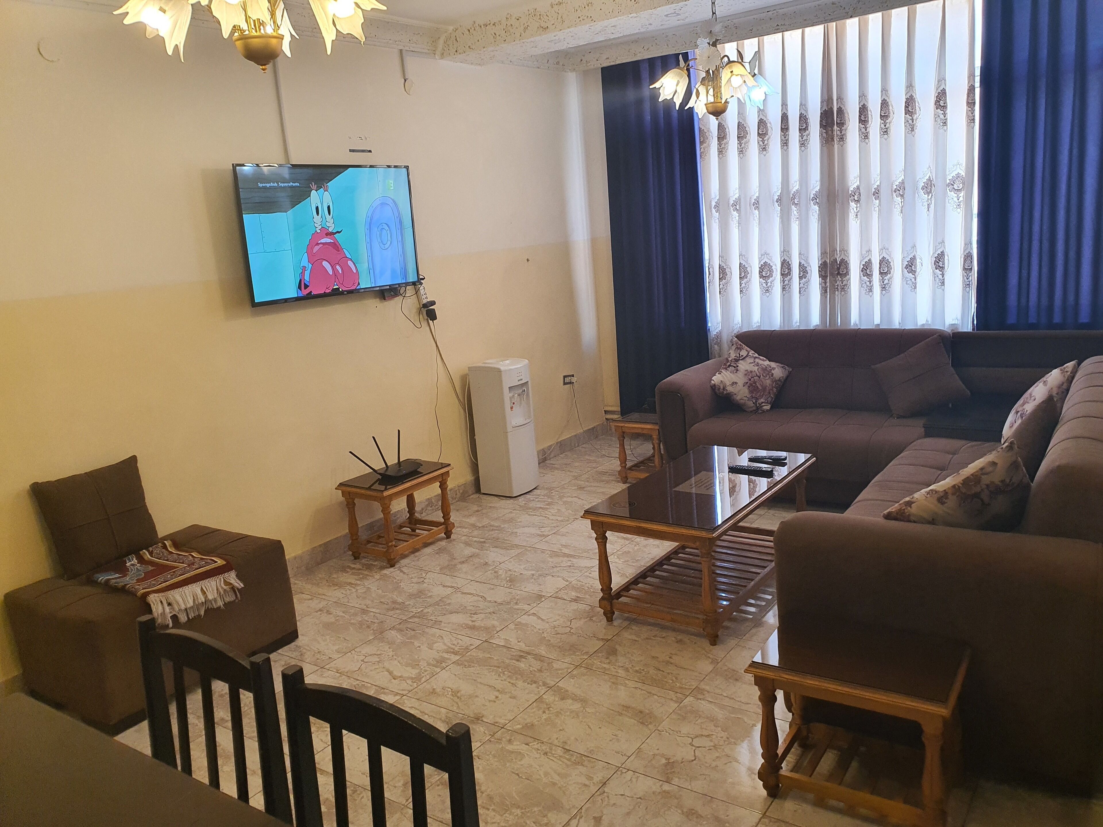 A living room with a sofa, a coffee table, a TV mounted on the wall, and a small table with a lamp.
