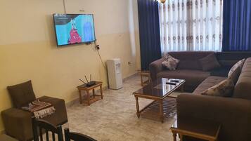 A living room with a sofa, a coffee table, a TV mounted on the wall, and a small table with a lamp.