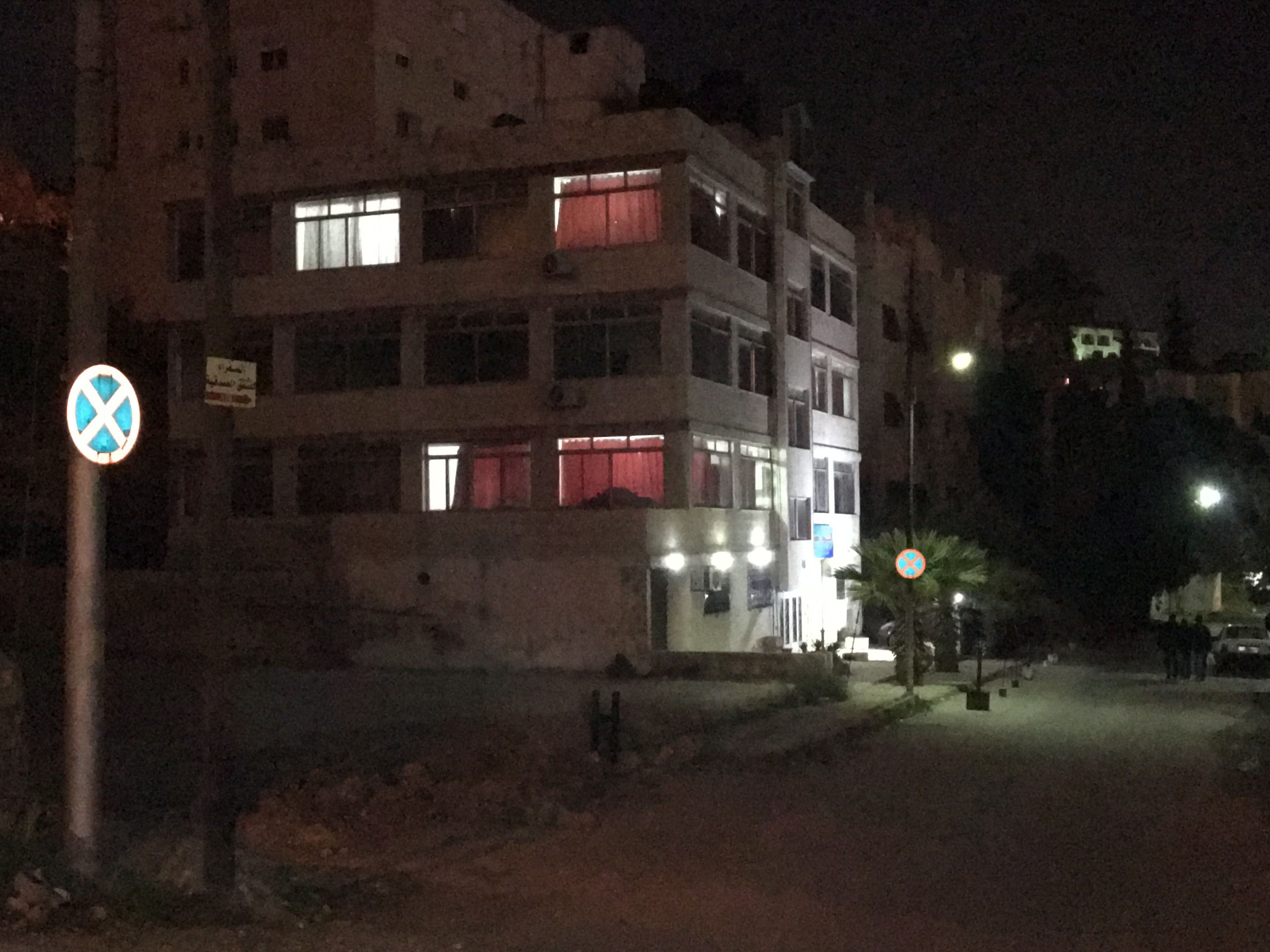 A multi-story building with illuminated windows and a visible "No Parking" sign.