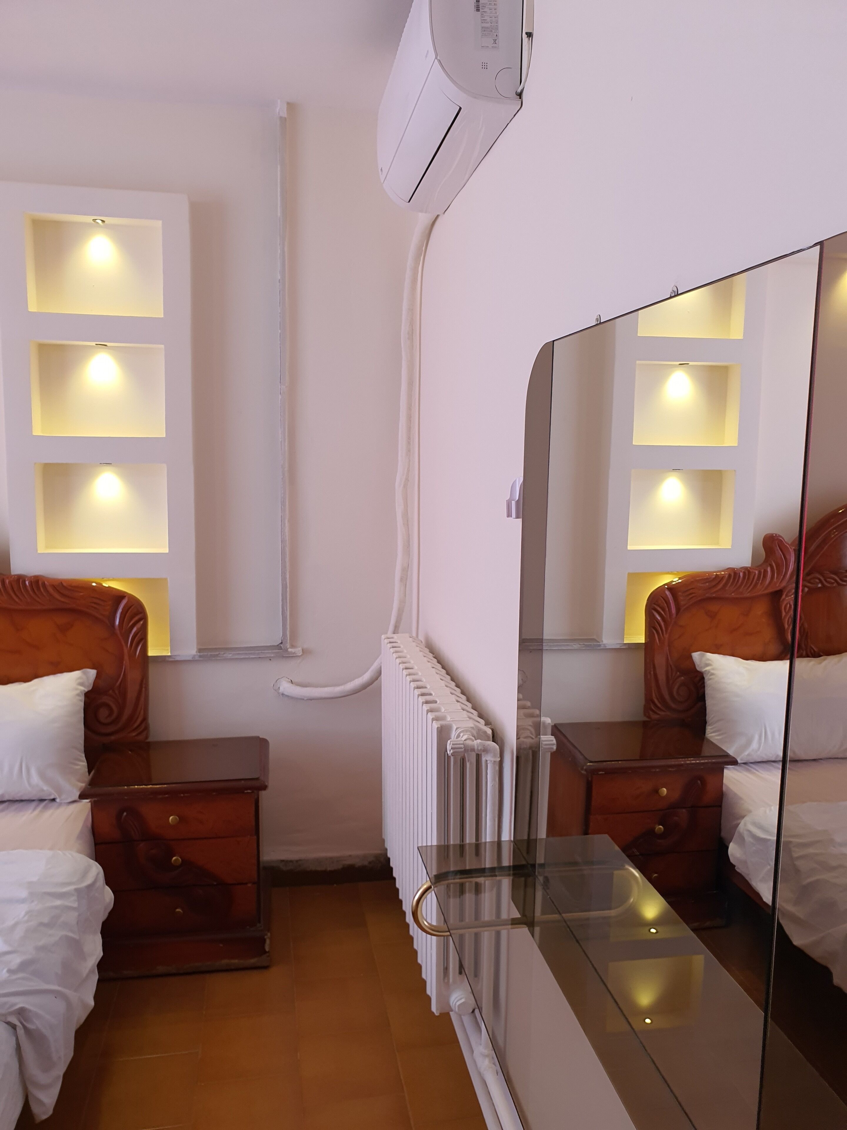 Ein Hotelzimmer mit einem Bett, Nachttischen, einem Spiegel, einem Heizkörper und Wandleuchten.
