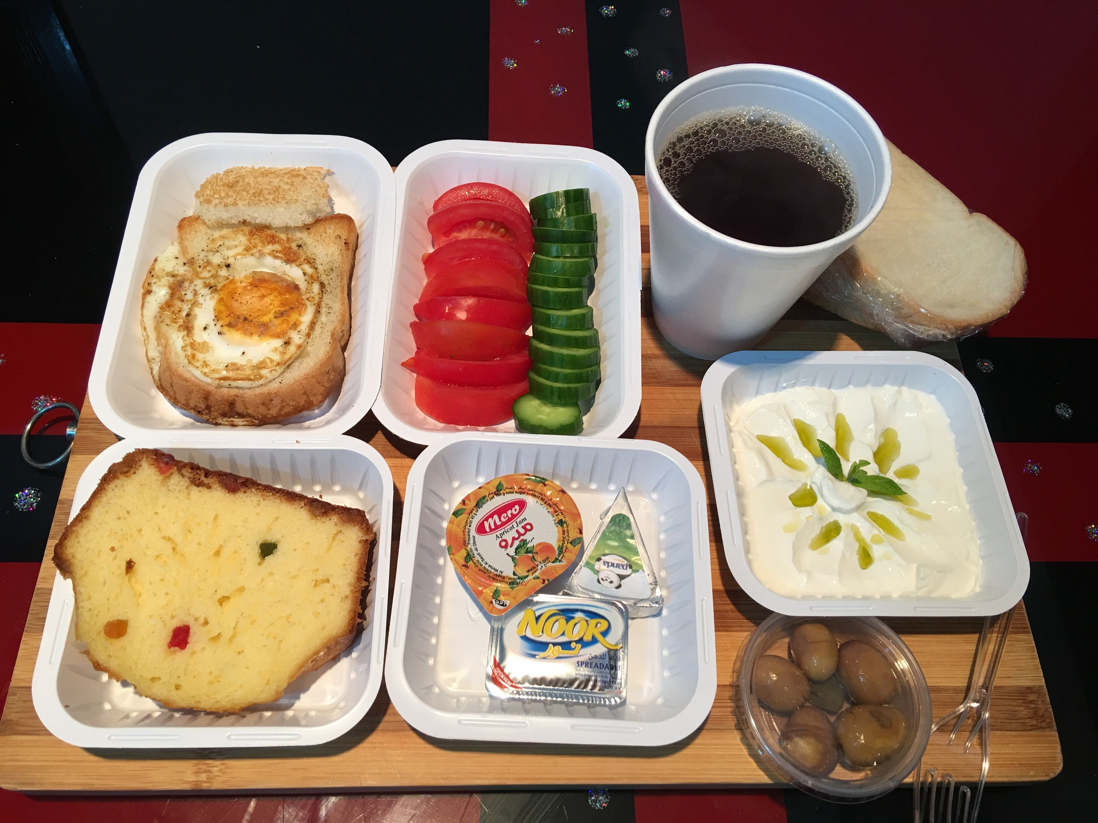 A meal tray with bread, eggs, tomatoes, cucumbers, yogurt, and olives.