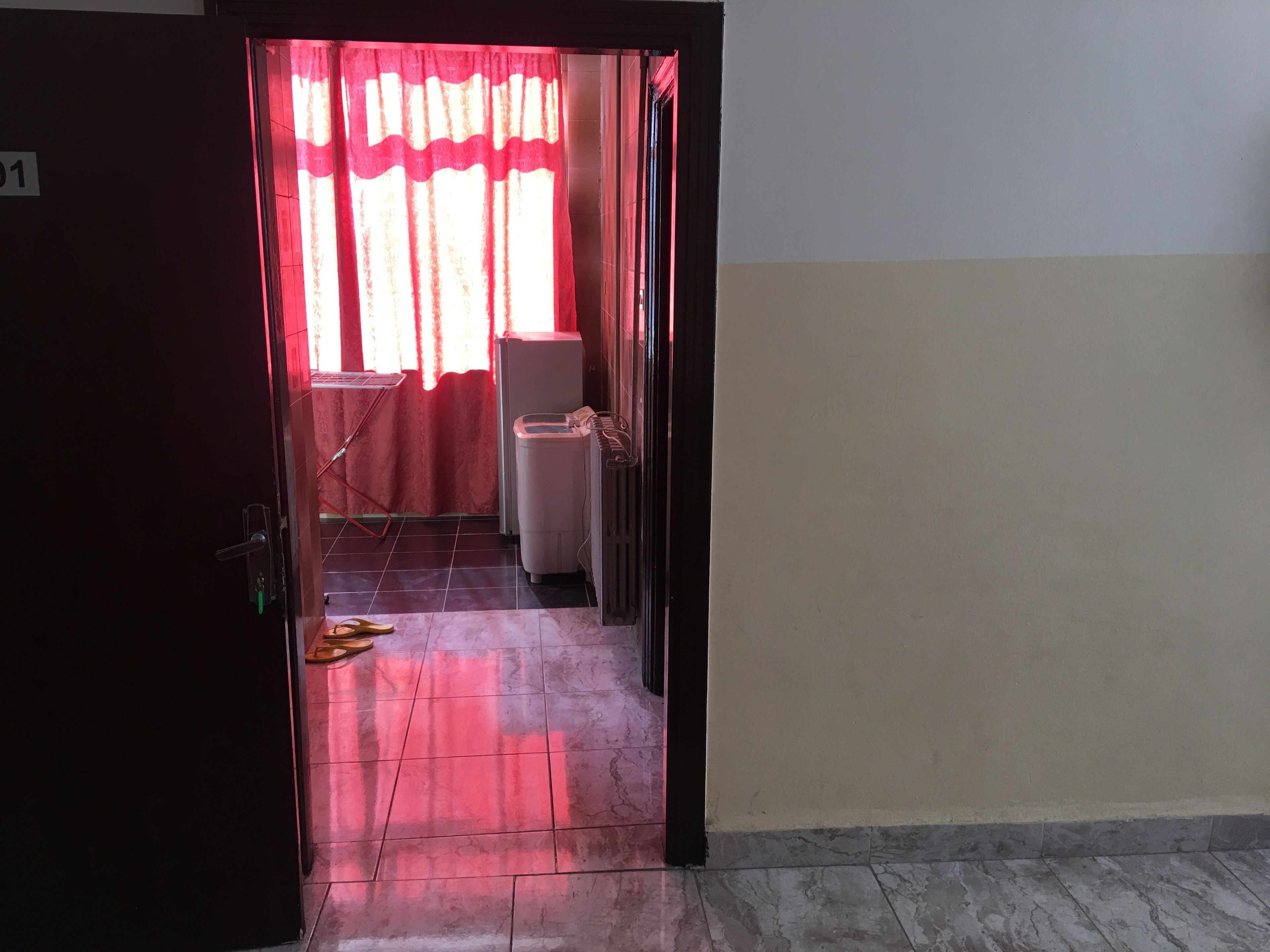 Un pasillo con suelo de baldosas, un radiador y una ventana con cortinas rojas.