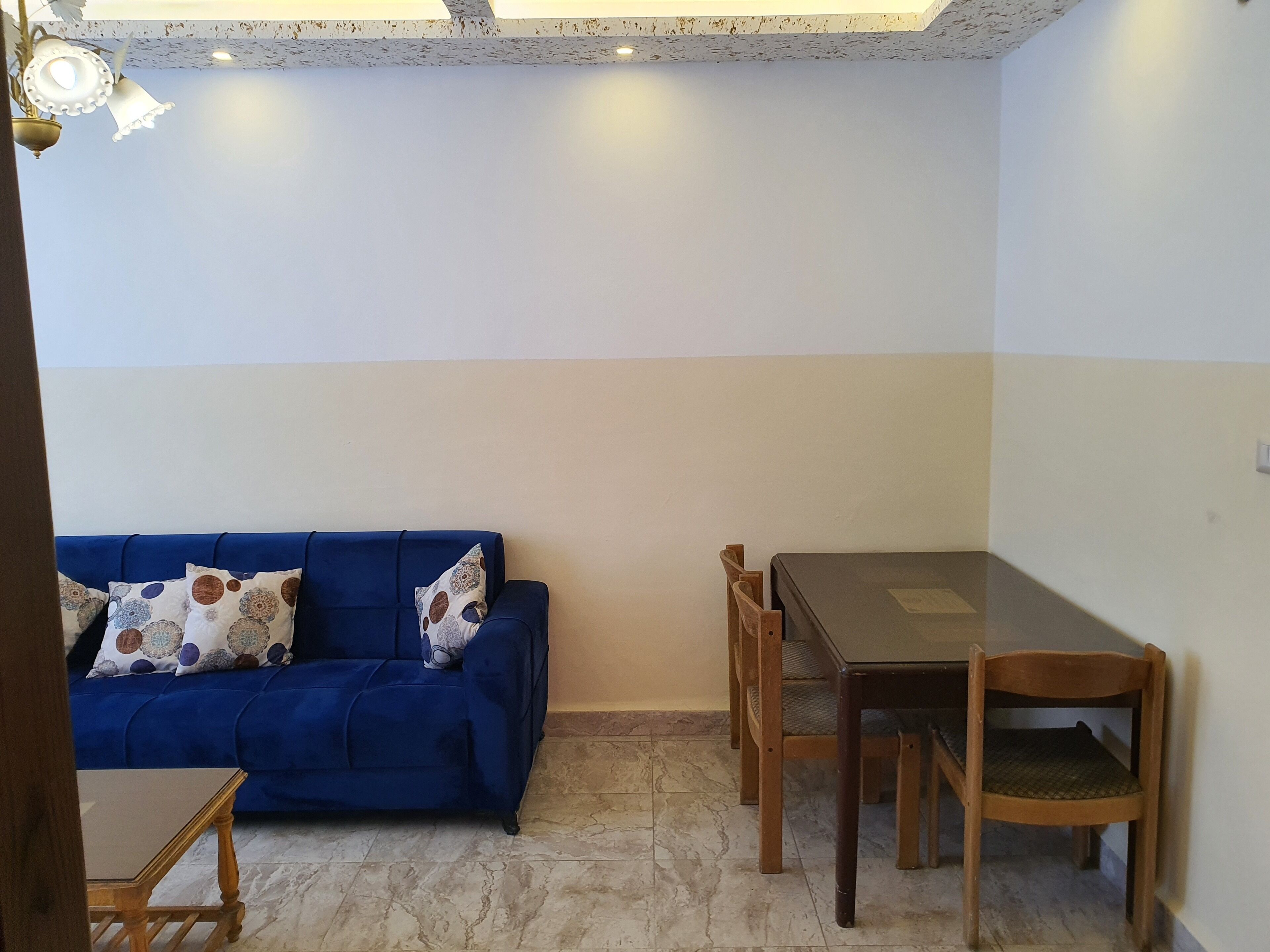 A room with a blue sofa, a wooden dining table with chairs, and a tiled floor.