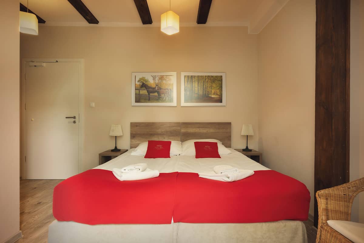 A hotel room with a large bed, two nightstands, a wooden headboard, a door, and two framed pictures on the wall.