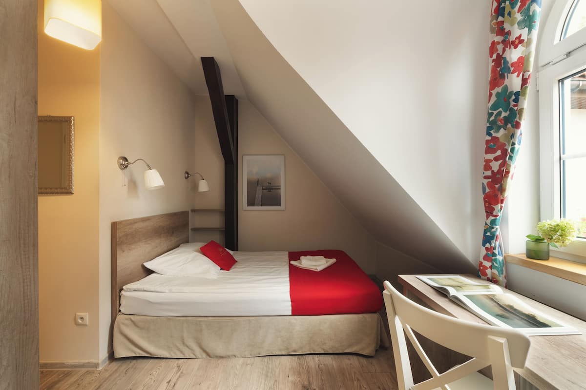 A bedroom with a bed, bedside table, lamp, and a window with curtains.