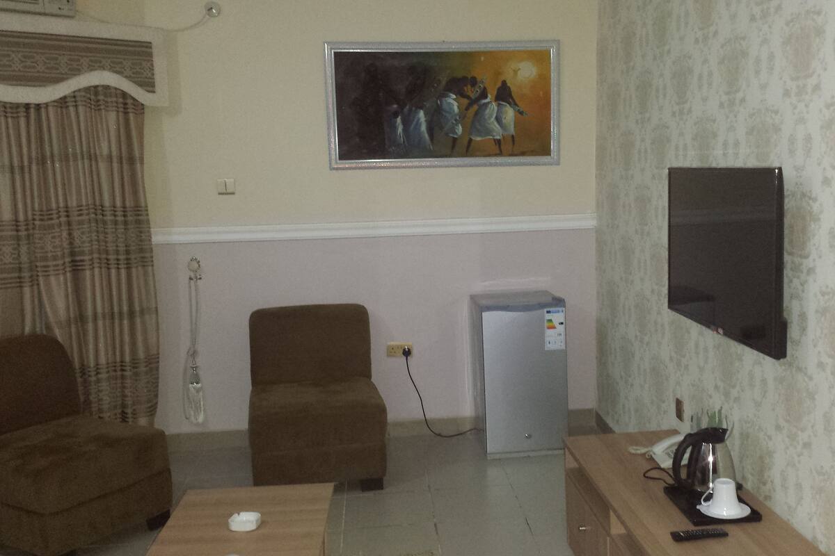 A living room with a sofa, a coffee table, a TV, a refrigerator, and a painting on the wall.