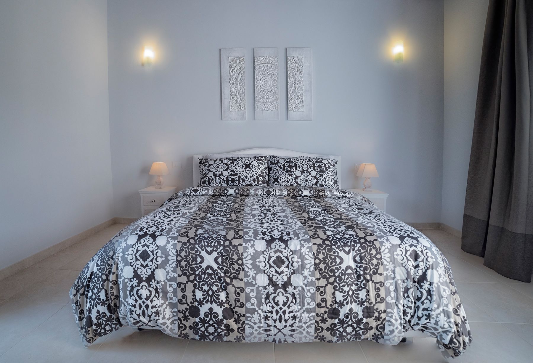 Une chambre à coucher avec une couvre-lit à motifs, deux lampes de chevet et des œuvres d’art décoratives accrochées au mur.