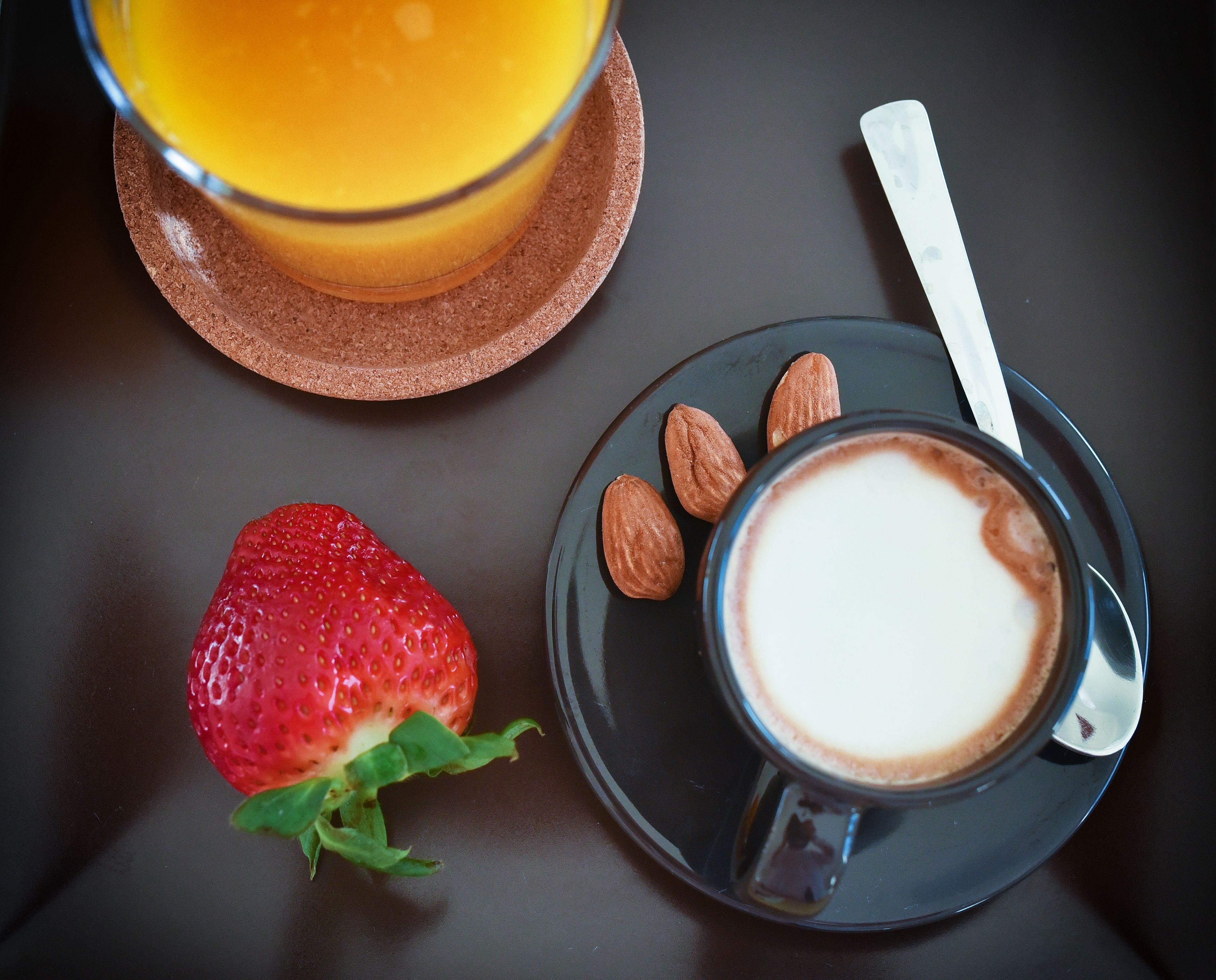 Taula amb un got de suc d'aranja, una tassa de cafè, una fresa i almendres.
