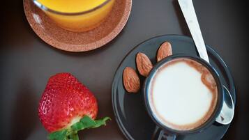 Taula amb un got de suc d'aranja, una tassa de cafè, una fresa i almendres.