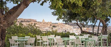 Un área de estar al aire libre con mesas y sillas, con vista a un paisaje urbano histórico con edificios destacados.