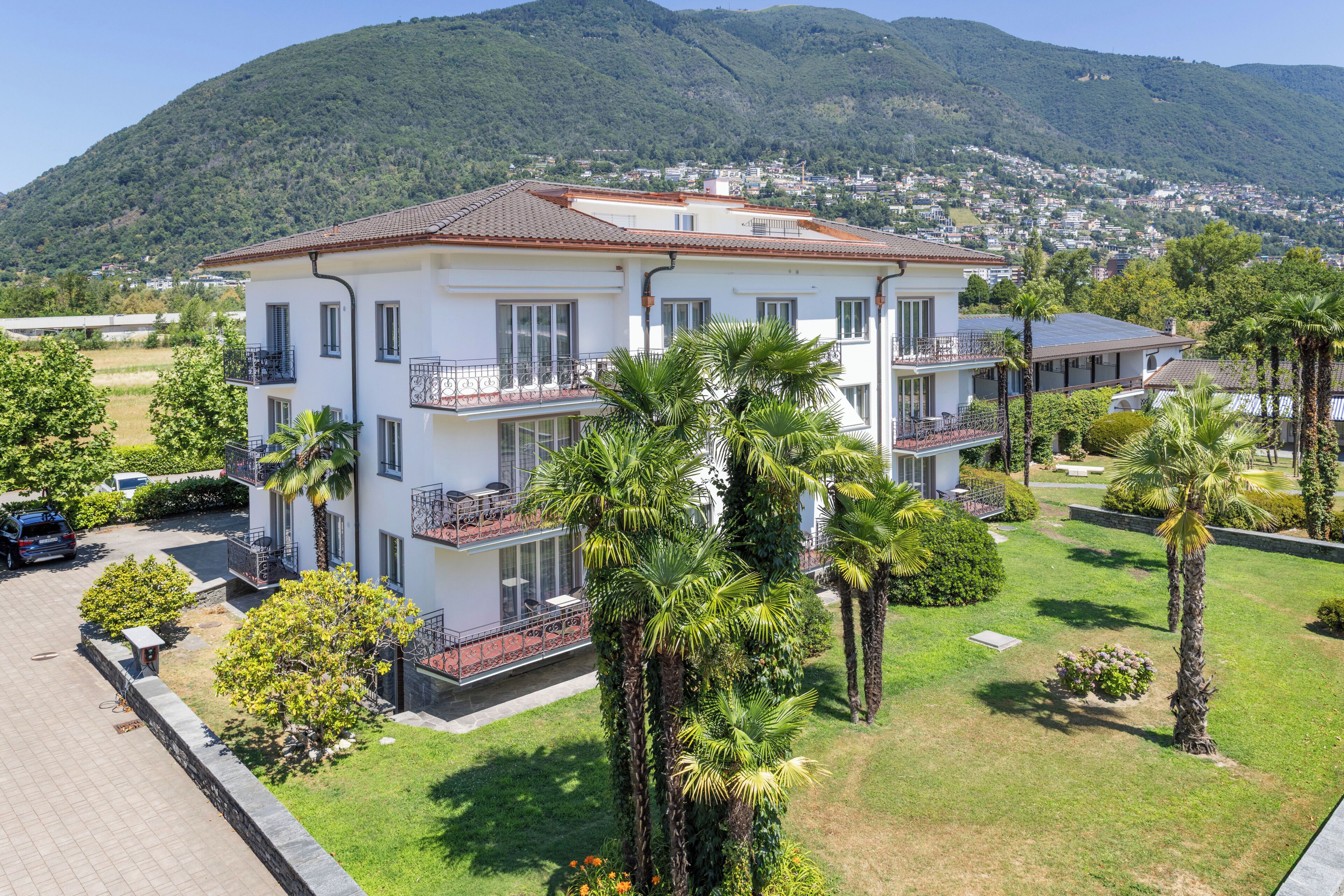 Un edificio de varios pisos con balcones, rodeado de vegetación y un paisaje montañoso.