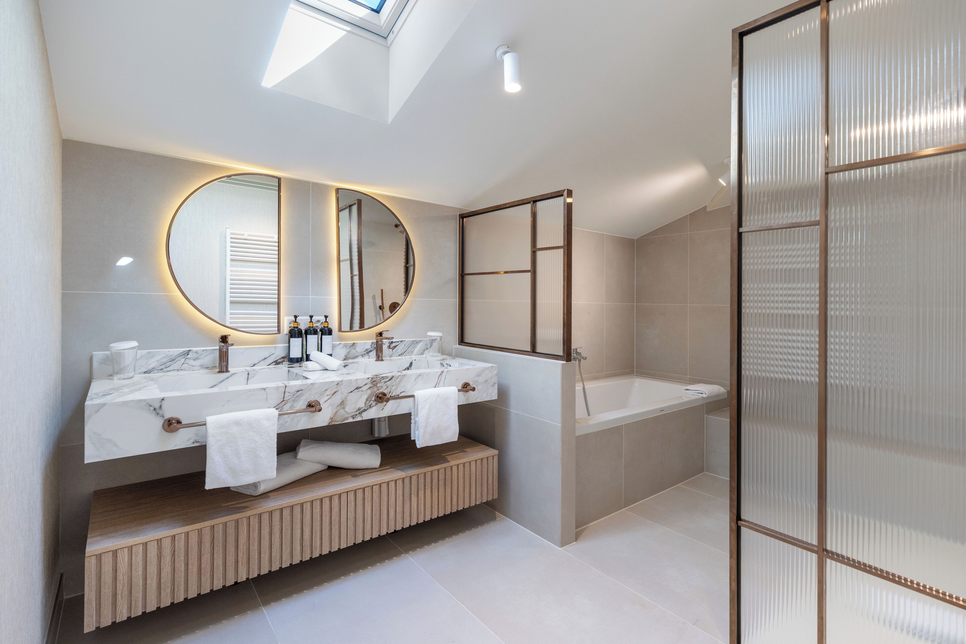 A modern bathroom with a skylight, a large mirror, a dual sink vanity, and a walk-in shower.