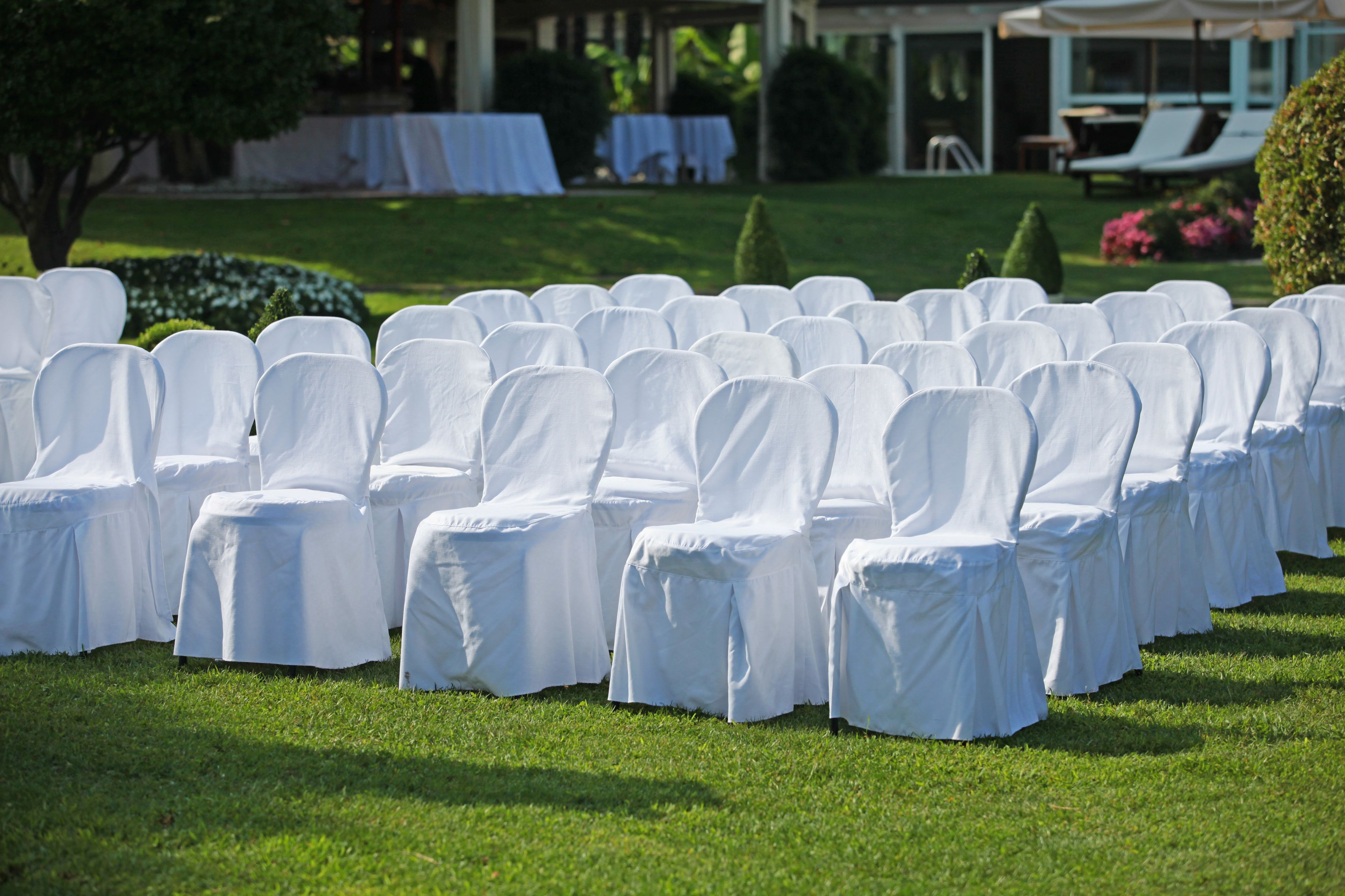 Rows of white chairs with tablecloths, arranged outdoors on a grassy area.