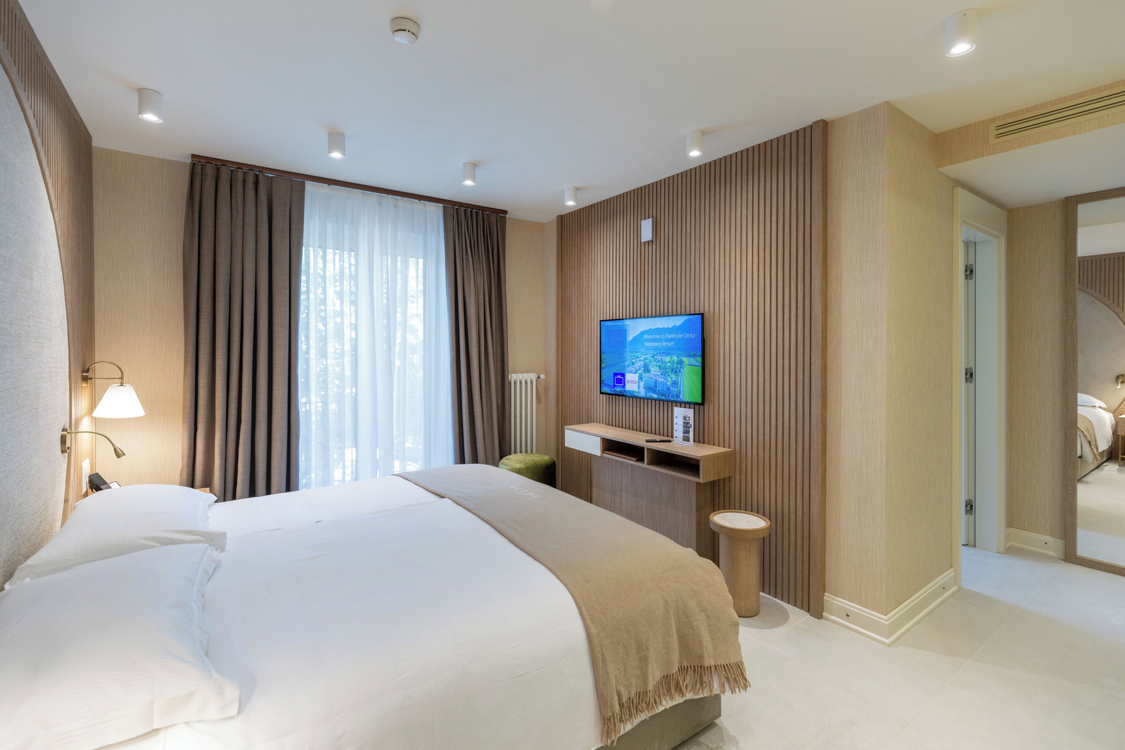 Habitación de hotel con una cama grande, un televisor montado en la pared y vistas al exterior a través de la ventana.