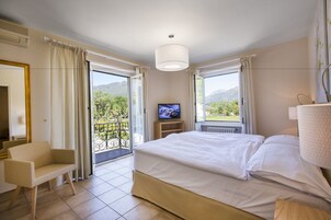 Habitación de hotel con cama, televisión, una silla y un balcón con vistas a las montañas.