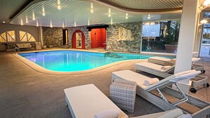 An indoor swimming pool with lounge chairs and a stone wall. - Villa Delta – Parkhotel Delta (Ascona)