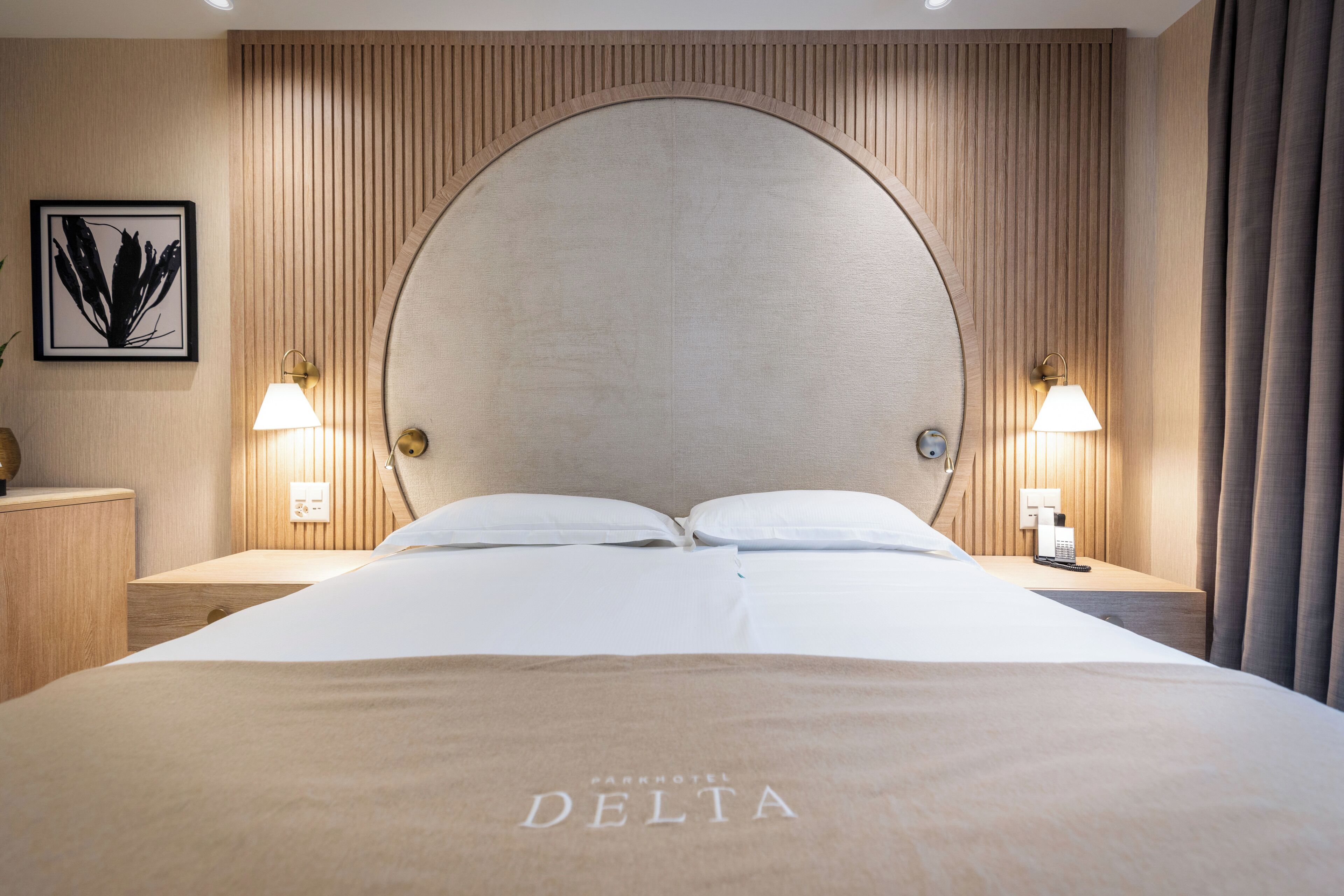 A hotel room with a large bed, two bedside lamps, a framed artwork, and a wall-mounted phone.