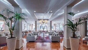 A spacious lobby with a polished marble floor, large potted plants, and a central seating area with sofas and a coffee table. - Villa Delta – Parkhotel Delta (Ascona)