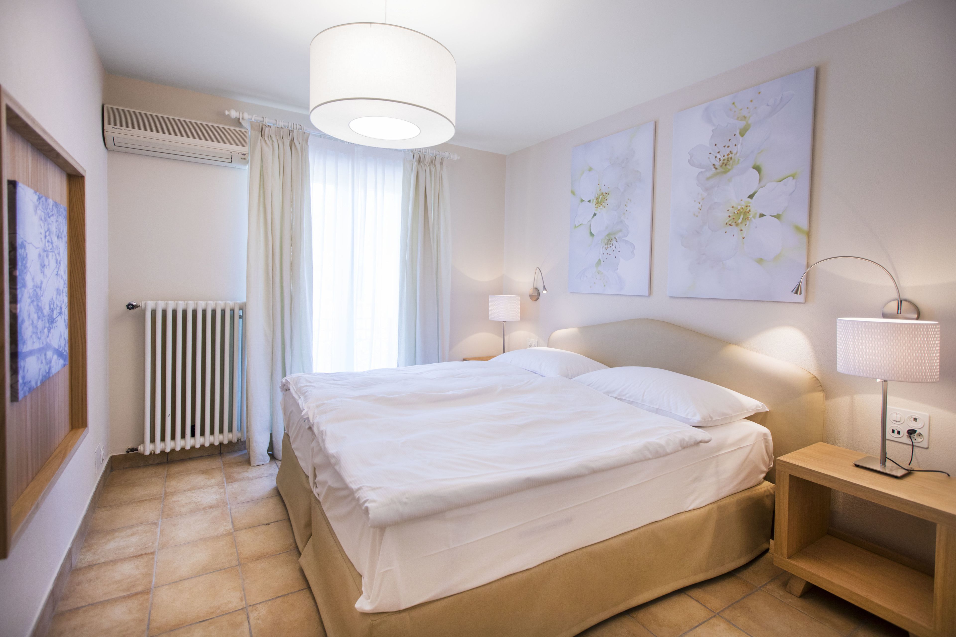 Un cuarto de hotel ordenado con una cama, lámparas de noche y obras de arte en las paredes.