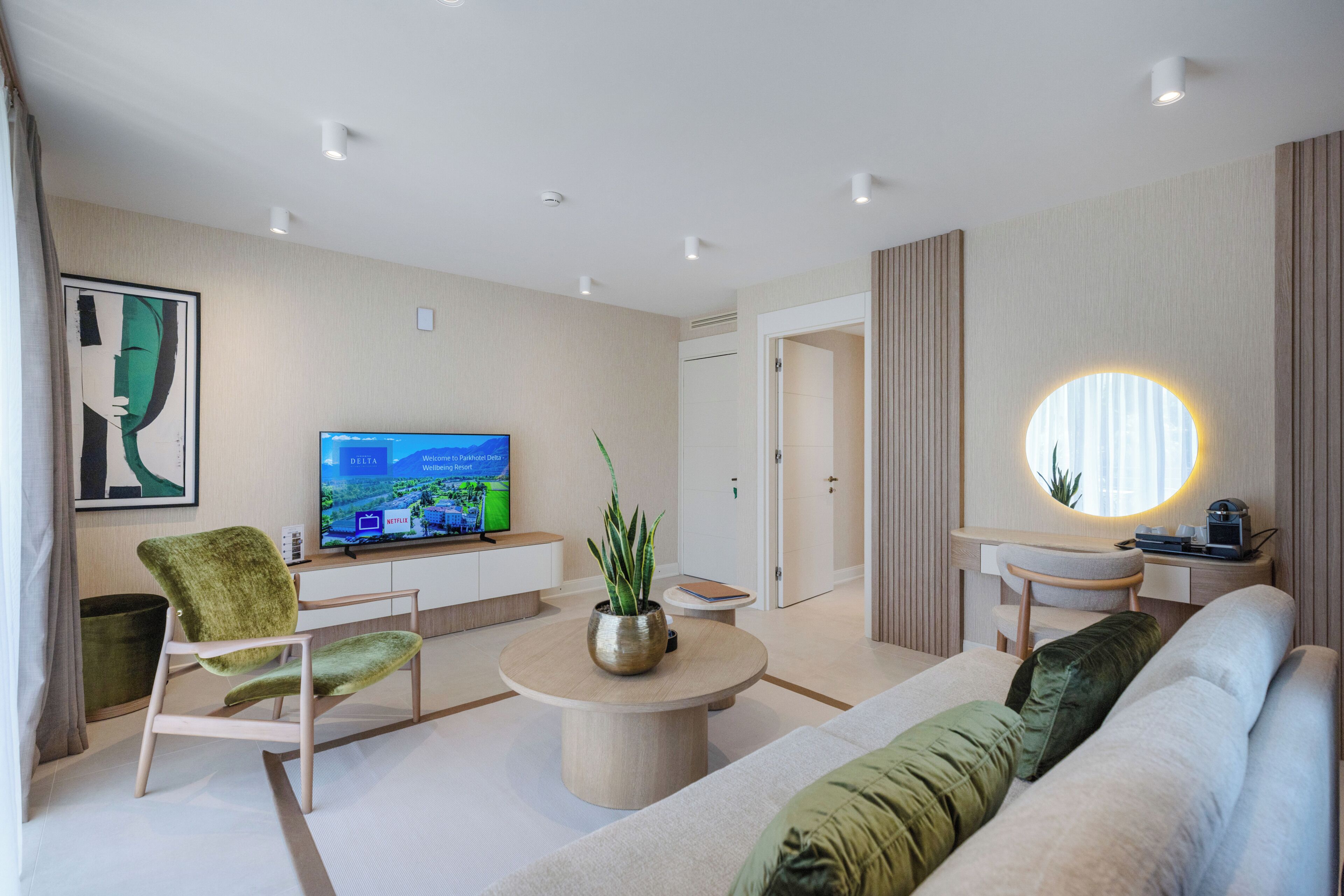 Une chambre d’hôtel moderne équipée d’un téléviseur à écran plat, d’une table ronde, d’un canapé, d’un fauteuil vert et d’une plante en pot.