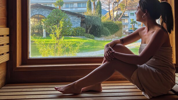 A person sitting by a window with a view of a building and greenery. - Villa Delta – Parkhotel Delta (Ascona)