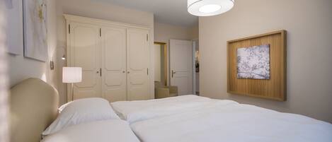 A hotel room with a large bed, a desk, a chair, a wardrobe, and a painting on the wall.
