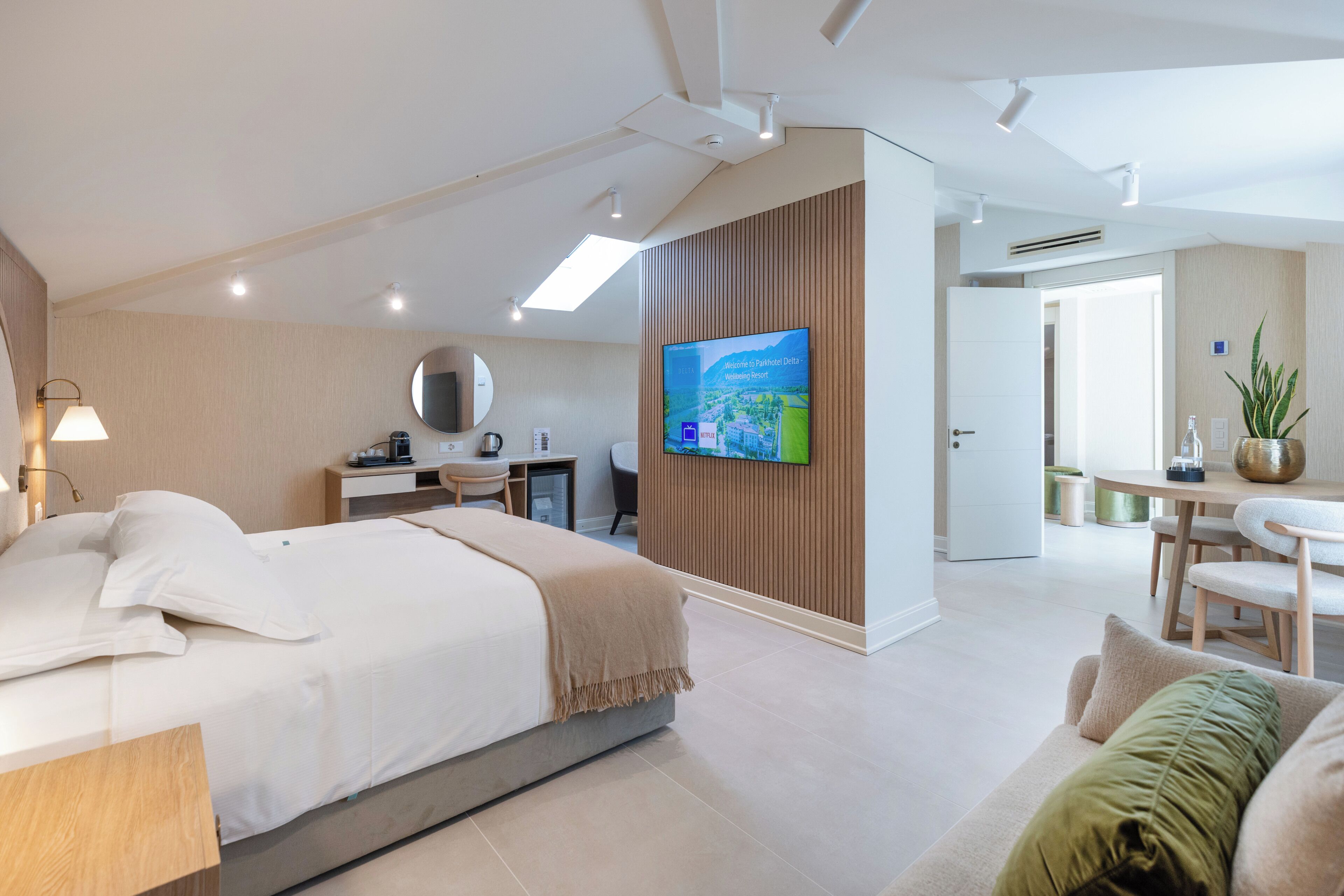 Una habitación de hotel moderna con cama, escritorio, silla, televisión y un área de comedor.