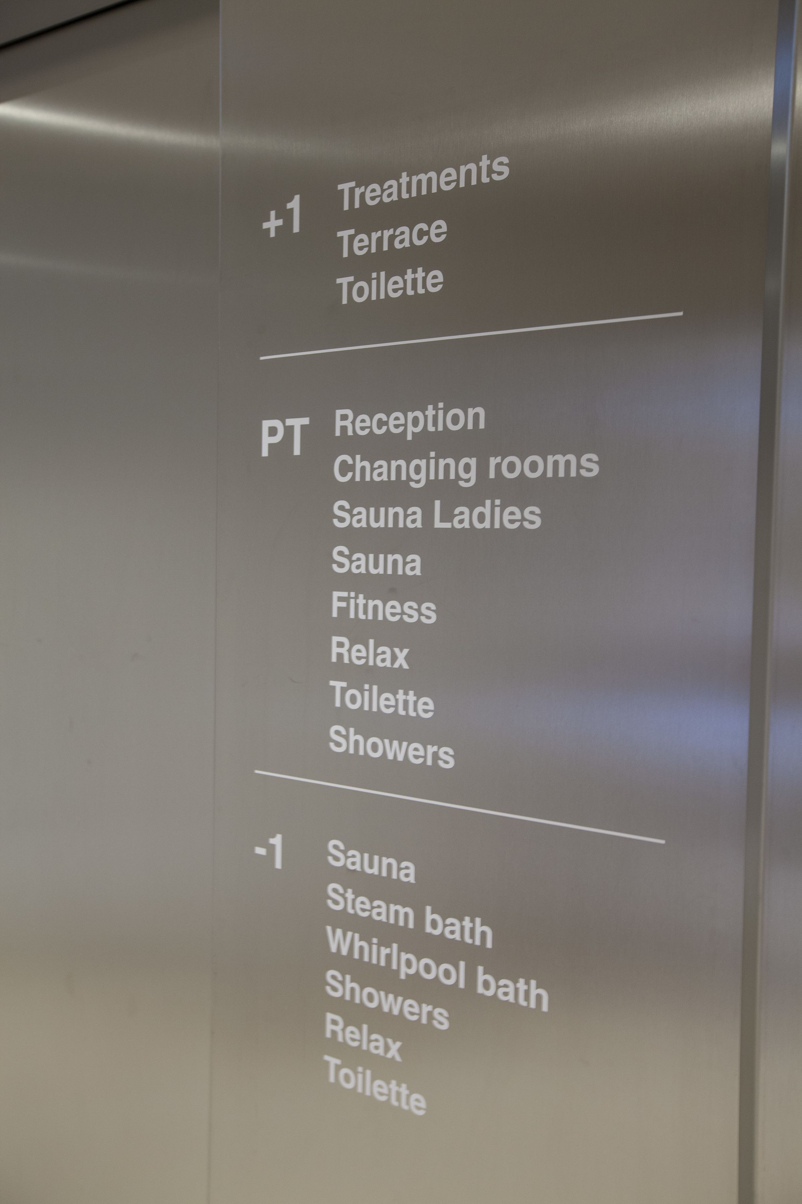 A sign listing hotel amenities including treatments, reception, changing rooms, saunas, fitness, relax areas, showers, and toilets.