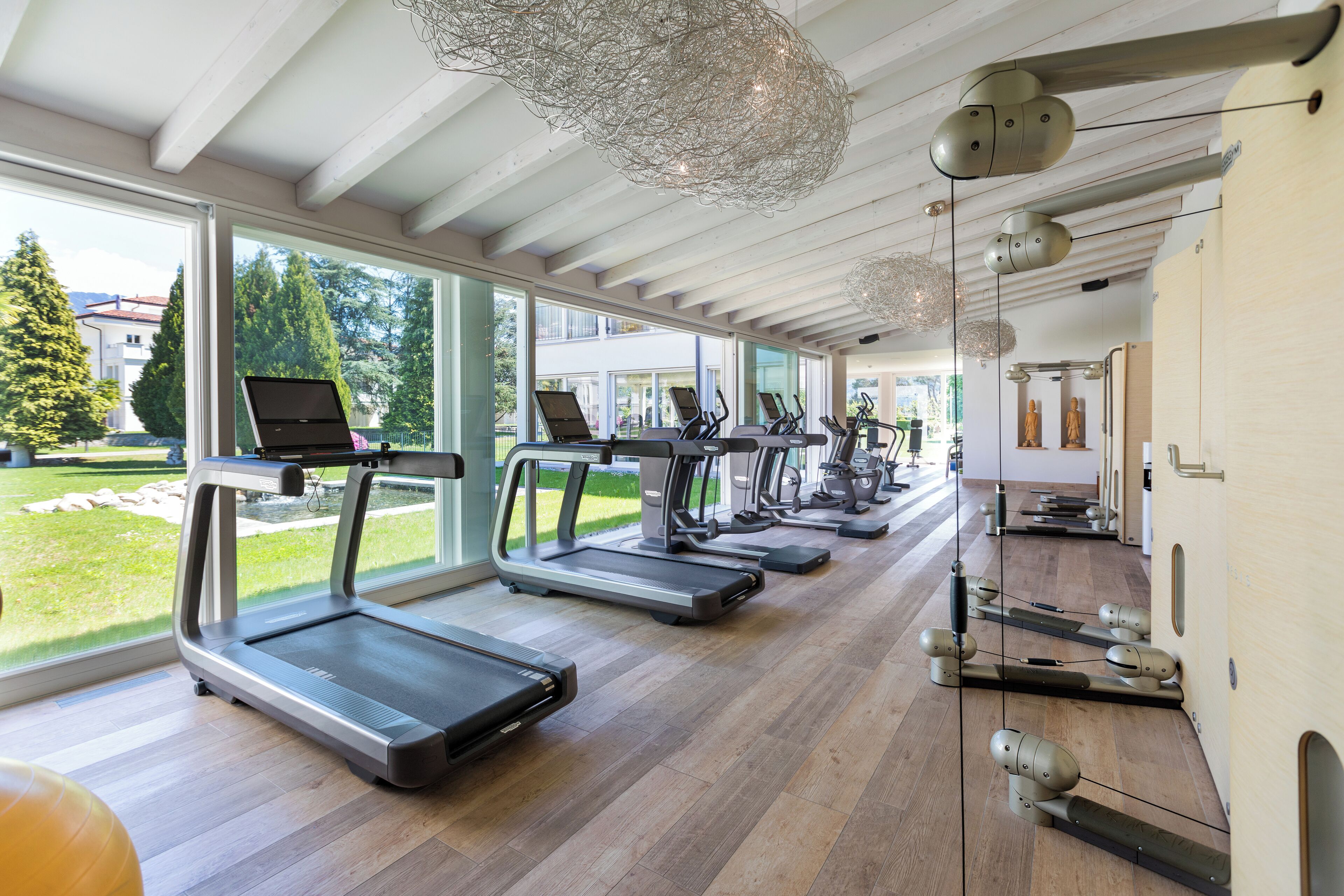 Een sportschool met loopbanden, hometrainers en een groot raam met uitzicht op de omgeving.