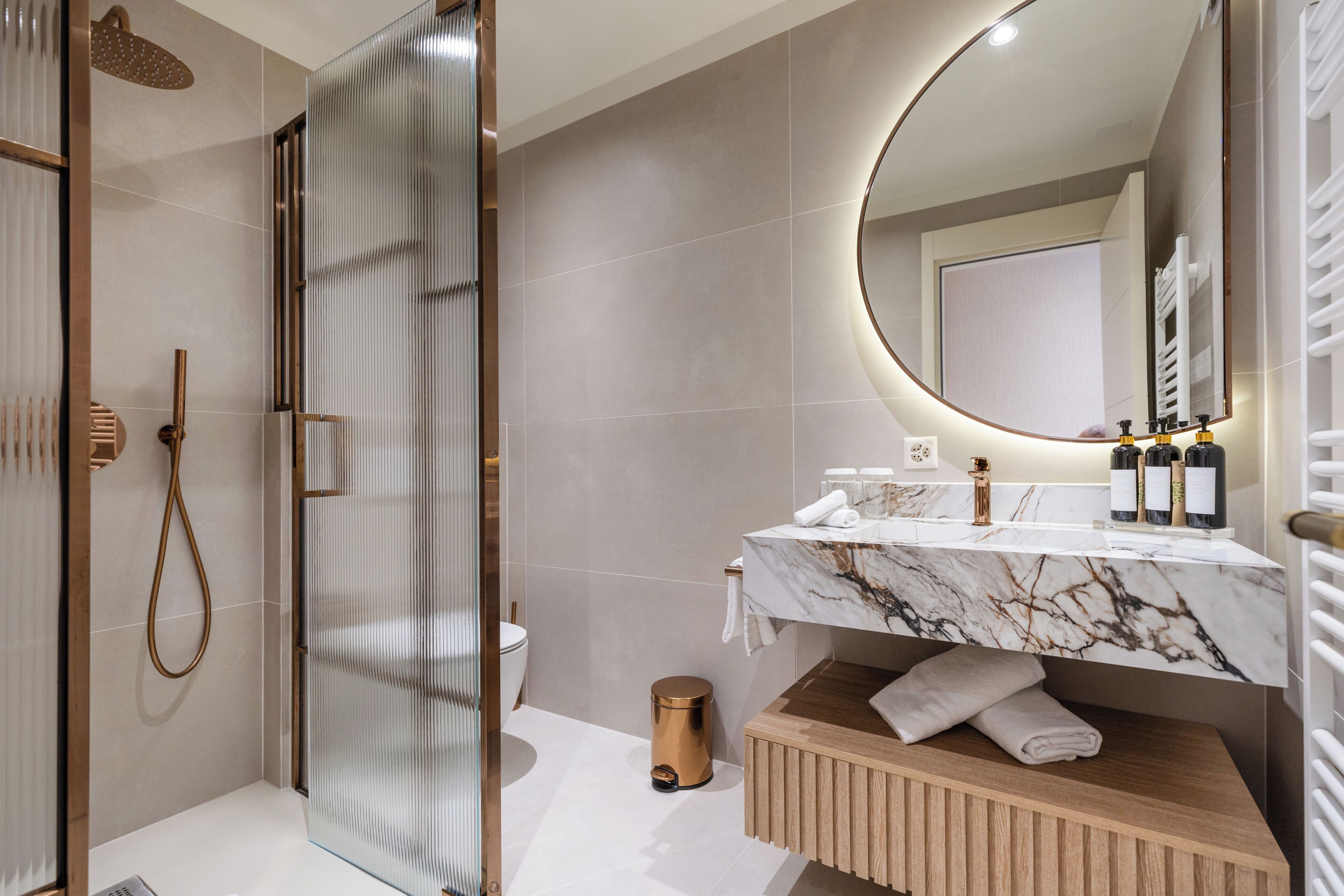 Un baño moderno con ducha envuelta en vidrio, lavamanos de mármol y tocador de madera.