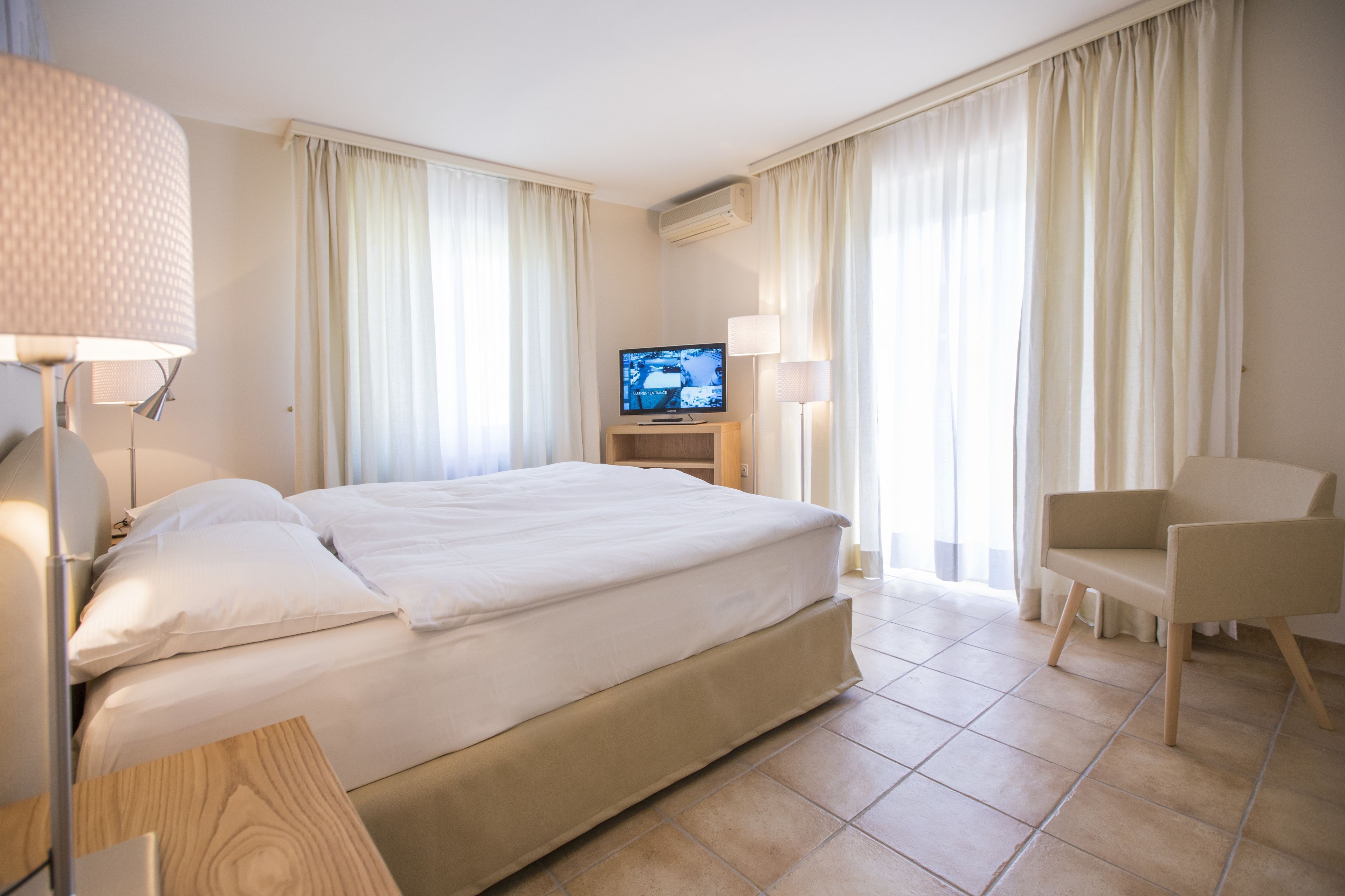 Een hotelkamer met een groot bed, een televisie, een stoel en gordijnen.