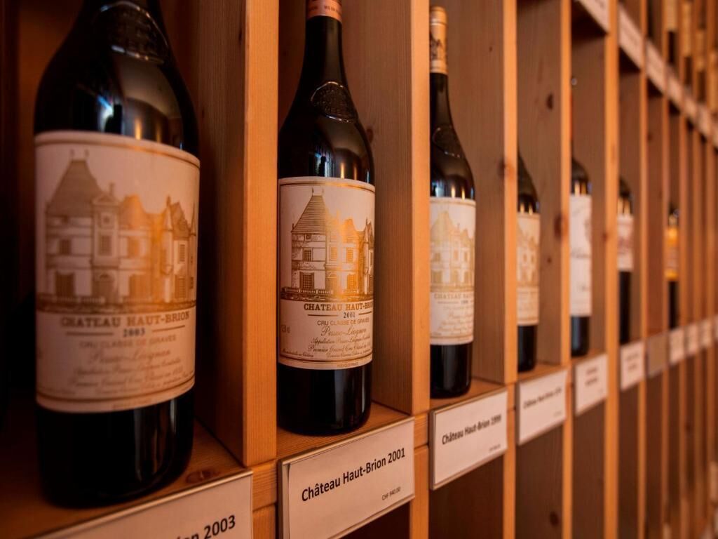 Una hilera de botellas de vino con etiquetas, cada una en un estante de madera con una etiqueta que indica el año 2003.