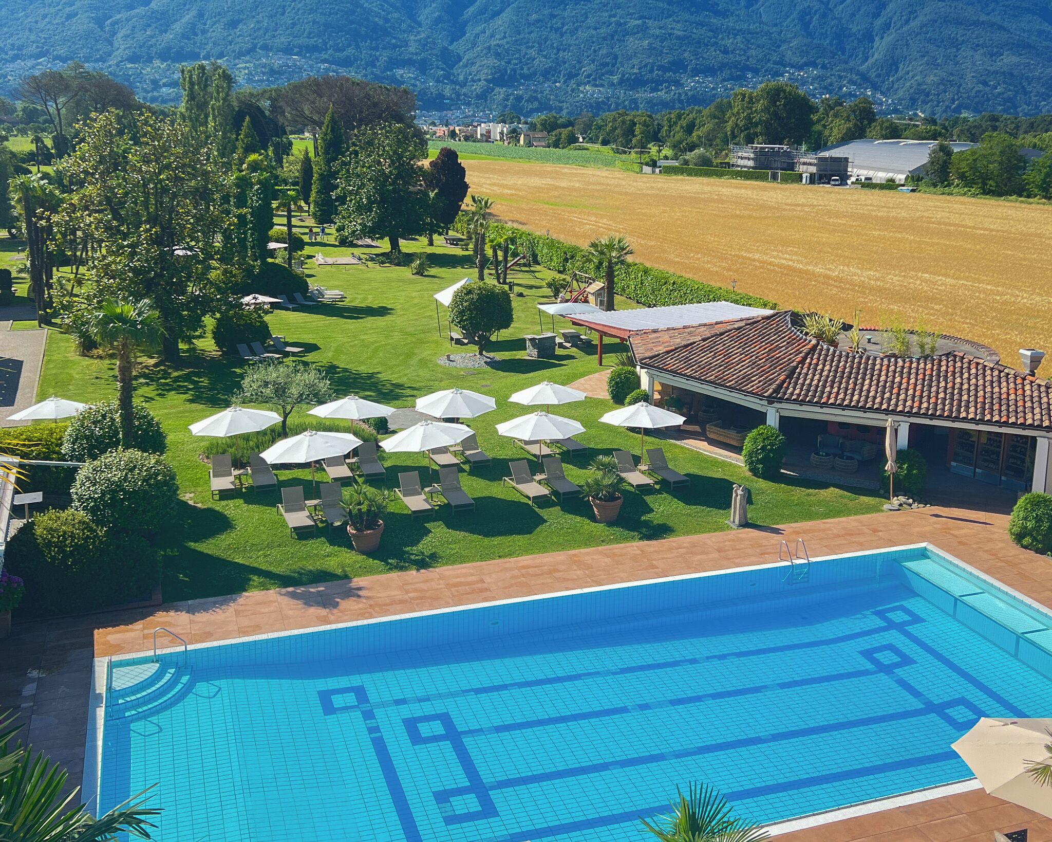 A swimming pool with lounge chairs and umbrellas, surrounded by a well-maintained lawn and a view of the countryside.