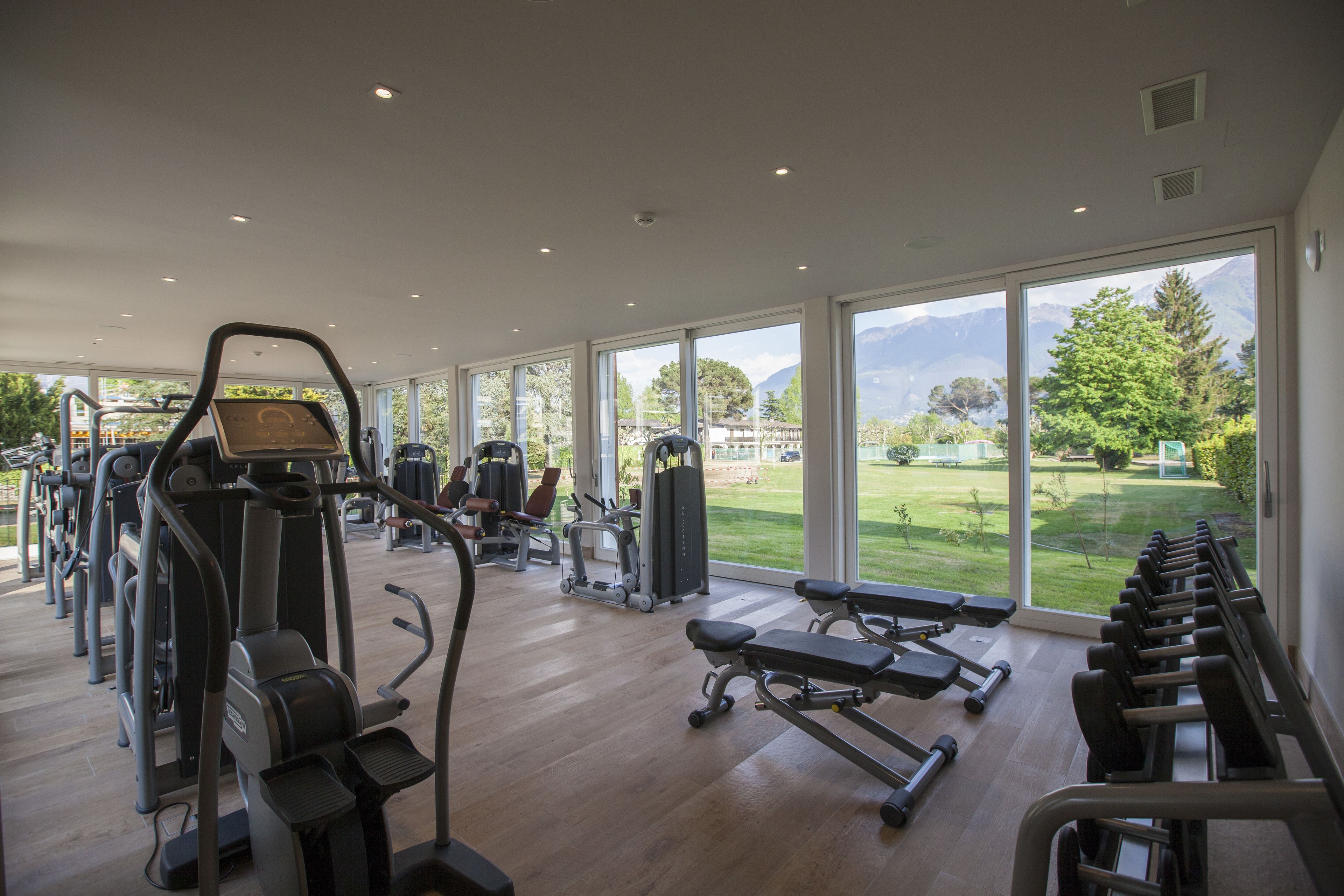 Un gimnasio con máquinas de cardio, bancos de pesas y vistas a un paisaje verde a través de amplias ventanas.