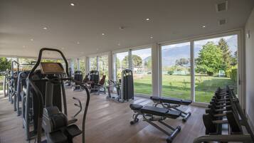 Un gimnasio con máquinas de cardio, bancos de pesas y vistas a un paisaje verde a través de amplias ventanas.