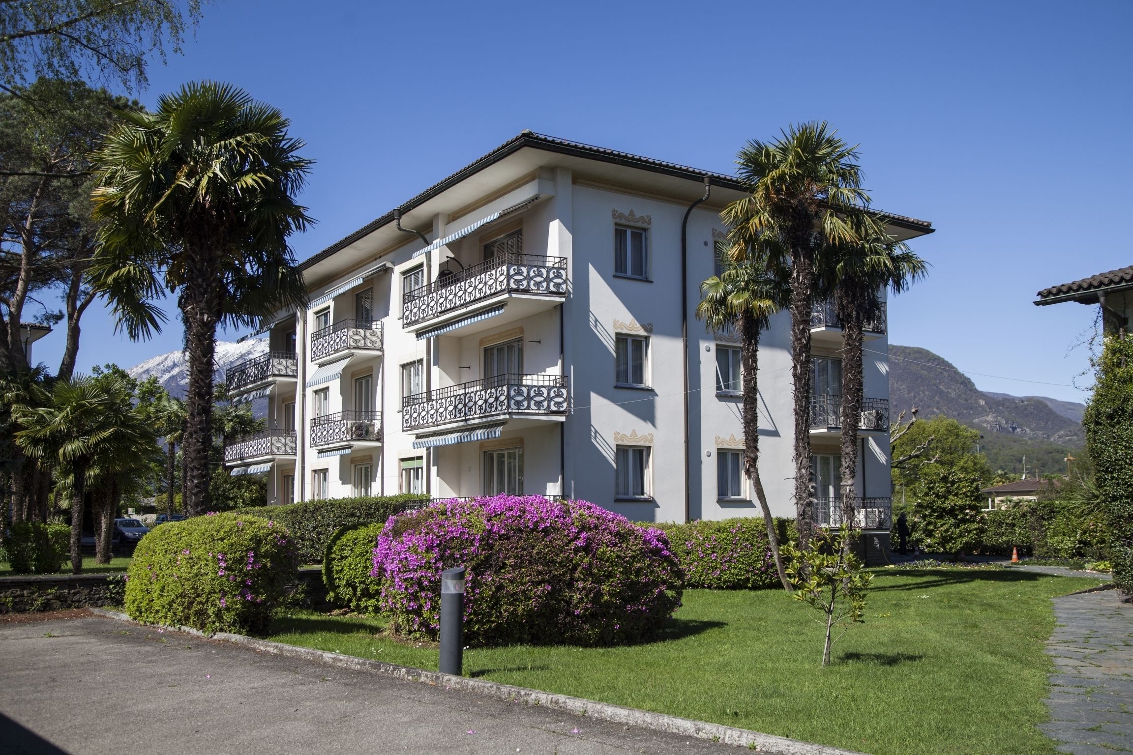 A multi-story building with balconies, surrounded by well-maintained greenery and palm trees.