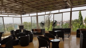 A spacious indoor area with large windows, wicker furniture, and ceiling fans. - Check Inn Hotel Abuja (Abuja)