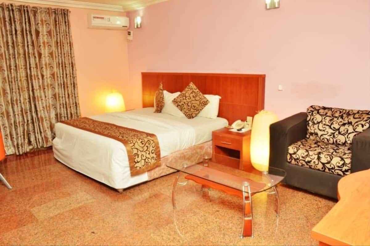 A hotel room with a bed, a nightstand, a lamp, a sofa, and a glass coffee table.