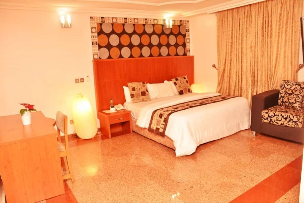 A hotel room with a bed, bedside tables, a desk, a chair, and a patterned wall.