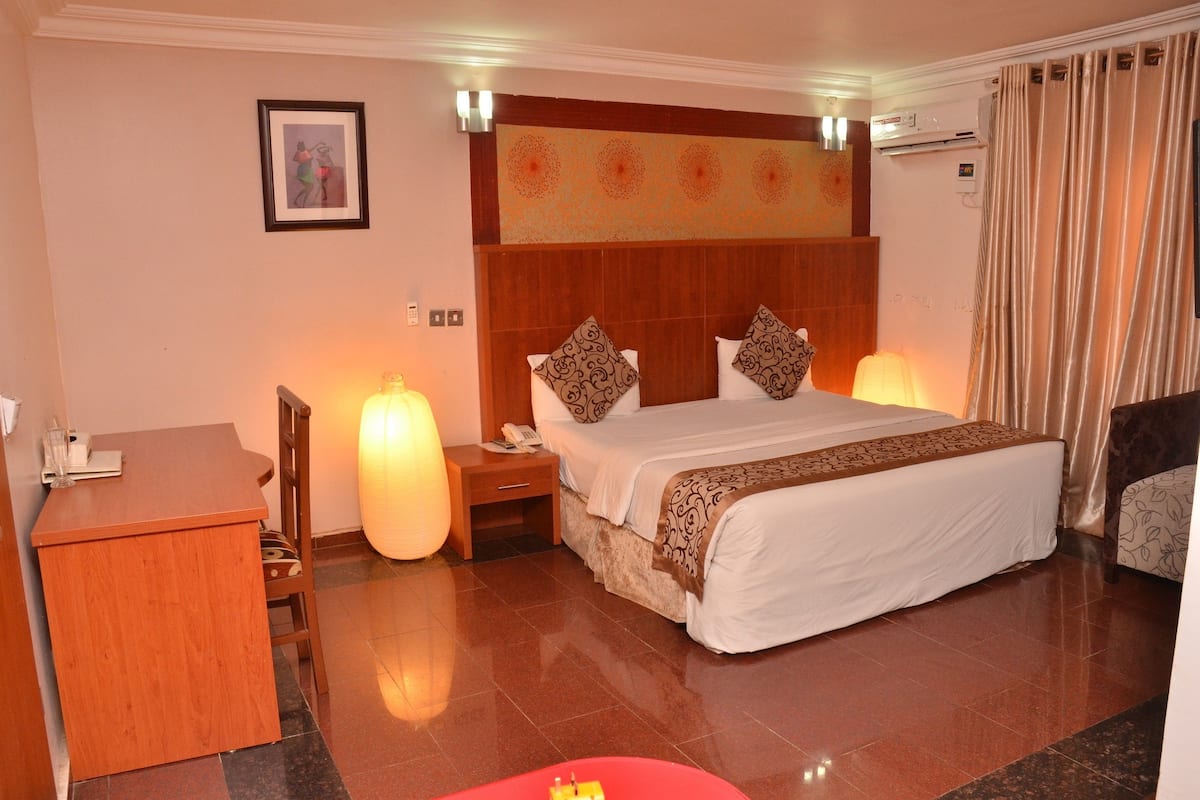 A hotel room with a bed, bedside tables, a desk, and a chair.